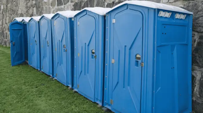 Row of blue portable toilets lined up on grass against a stone wall for event sanitation in Raleigh, NC