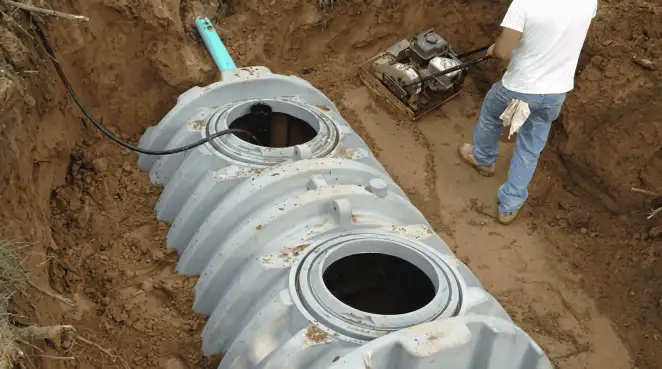 Septic tank installation showing a technician compacting soil around a new poly septic tank in an excavation pit in Raleigh, NC